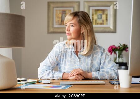 Porträtaufnahme einer selbstbewussten Geschäftsfrau, die am Schreibtisch sitzt und bei der Arbeit von zu Hause aus nachdenklich schaut. Stockfoto