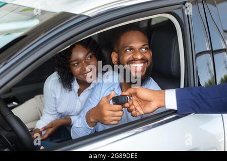 Glückliches Afroamerikanisches Paar, Das Schlüssel Vom Verkäufer Nach Dem Kauf Des Neuen Autos Nimmt Stockfoto