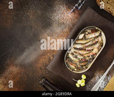 Horizontal, Lebensmittelzusammensetzung mit einer offenen Dose Baltic Sprotten mit Gewürzen, einer Gabel, einer Flasche dunklem Bier und Roggenbrot auf altem braunen Hintergrund mit pl Stockfoto