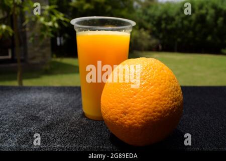 Citrus Malta Saft in transparentem Glas serviert mit Malta Obst auf dem Tisch. Natur Hintergrund offenen Bereich Umgebung mit grünen Bäumen verschwommen backgrou Stockfoto