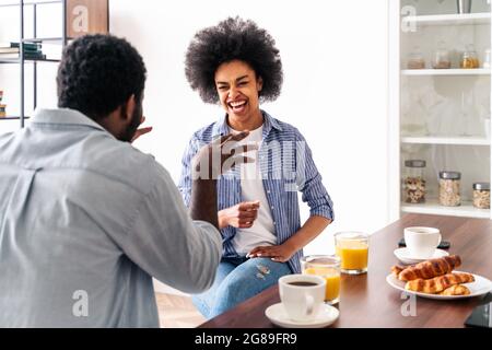 Wunderschönes afro-amerikanisches Paar, das zu Hause zusammen frühstückte - fröhliches schwarzes Paar, das morgens Zeit miteinander verbringt Stockfoto
