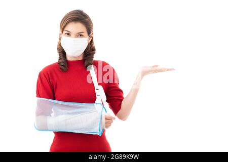 Schöne asiatische Frau mit gebrochenem Arm und Verband tragen chirurgische schützende Hygienemaske stehend isoliert auf weißem Hintergrund mit Smiley Gesicht. Poi Stockfoto
