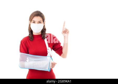 Schöne asiatische Frau mit gebrochenem Arm und Verband tragen chirurgische schützende Hygienemaske stehend isoliert auf weißem Hintergrund mit Smiley Gesicht. Poi Stockfoto
