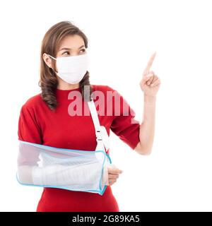 Schöne asiatische Frau mit gebrochenem Arm und Verband tragen chirurgische schützende Hygienemaske stehend isoliert auf weißem Hintergrund mit Smiley Gesicht. Poi Stockfoto