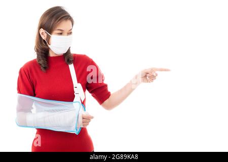 Schöne asiatische Frau mit gebrochenem Arm und Verband tragen chirurgische schützende Hygienemaske stehend isoliert auf weißem Hintergrund mit Smiley Gesicht. Poi Stockfoto