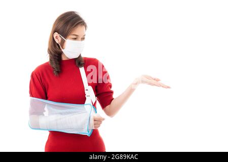 Schöne asiatische Frau mit gebrochenem Arm und Verband tragen chirurgische schützende Hygienemaske stehend isoliert auf weißem Hintergrund mit Smiley Gesicht. Poi Stockfoto