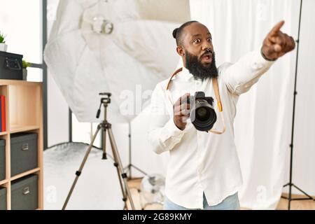 afroamerikanischer Fotograf Mann, der im Fotostudio arbeitet, zeigt mit dem Finger überrascht voraus, offener Mund erstaunt Ausdruck, etwas auf dem f Stockfoto