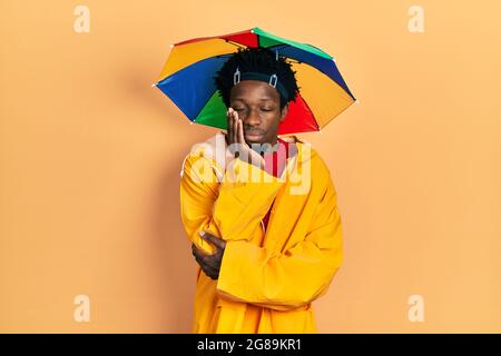 Junger afroamerikanischer Mann mit gelbem Regenmantel, der dachte, er sei müde und langweilen mit Depressionen und gekreuzten Armen. Stockfoto