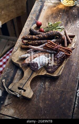 Von oben von verschiedenen geräucherten Wildfleischwürsten und frischem Rettich auf Schneidebrett in der Nähe von Pint Bier in rustikalem Restaurant platziert Stockfoto