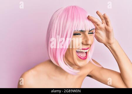 Junger Mann trägt Frau Make-up trägt rosa Perücke sehr glücklich und lächelnd suchen weit weg mit Hand über Kopf. Suchkonzept. Stockfoto