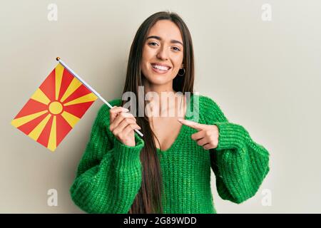 Junge hispanische Mädchen hält mazedonische Flagge lächelnd glücklich zeigt mit Hand und Finger Stockfoto