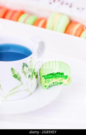 Porzellanbecher mit blauem Thai-Schmetterlingsblütentee und gebissenen grünen Makronen oder Makronen Stockfoto