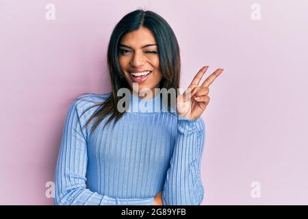 Junge lateinische transsexuelle Transgender Frau in lässigen Kleidern lächelnd mit glücklichen Gesicht zwinkend an der Kamera tun Siegeszeichen. Nummer zwei. Stockfoto