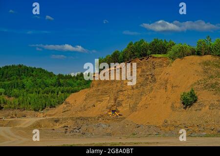 Sandsteinbruch mit einem gelben Traktor im Inneren. Bagger arbeiten an Erdarbeiten im Tagebau Stockfoto