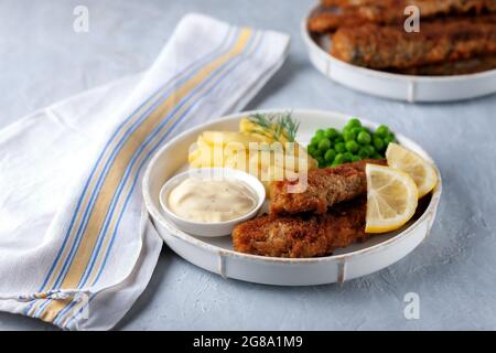 Gebratener Fisch mit grünen Erbsen, Zitrone und gebratenen Kartoffeln Stockfoto