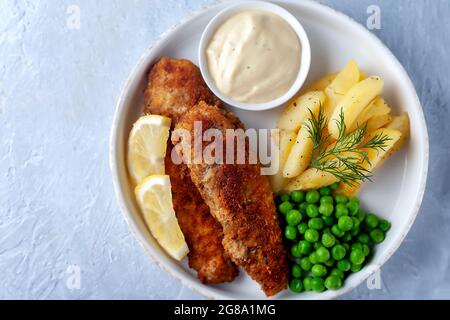 Gebratener Fisch mit grünen Erbsen, Zitrone und gebratenen Kartoffeln Stockfoto