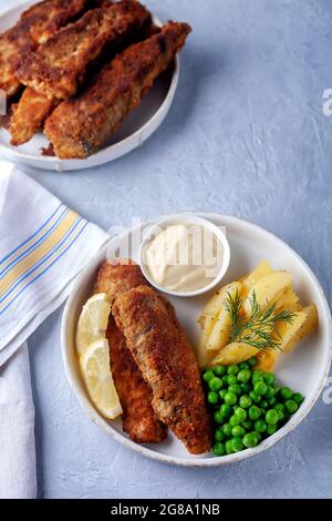 Gebratener Fisch mit grünen Erbsen, Zitrone und gebratenen Kartoffeln Stockfoto