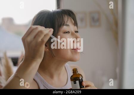 Junge asiatische smilling Frau feuchtigkeitsspendende Gesicht mit Öl. Nachhaltiger Lebensstil. Skic Care-Konzept Stockfoto