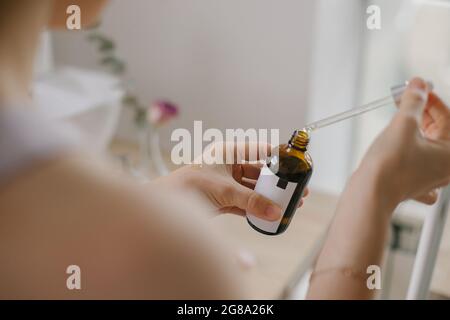 Frau hält ein geöffnetes Hautpflegeprodukt in einer Glasflasche mit Pipette, während sie zu Hause die morgendliche Schönheitsroutine macht Stockfoto