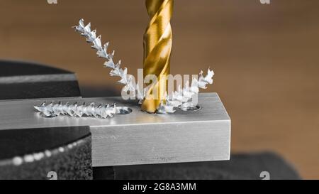 Nahaufnahme von spiralförmig gerilltem Bohrer und Schneckenspan im Metallteil auf braunem Hintergrund. Bohrloch in Aluminiumprofil, eingespannt in schwarzem Schraubstock. Stockfoto