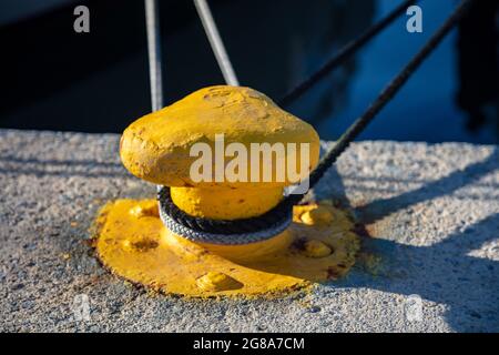 Festmachen Poller Konzept. Seile mit Drehknöpfen auf gelbem Stahlbollard verdreht. Gesicherte Jachten am Hafen Marina Kai, Griechenland. Nahaufnahme, sonnig Stockfoto