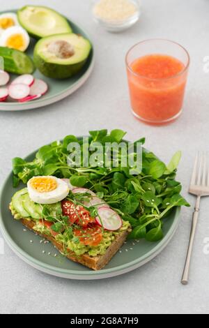 Gesundes, leckeres Frühstück, Sandwich mit Avocado und Lachs, Gurken und Radieschen sowie Mikrogemüse aus Erbsen mit gekochtem Ei und Maissalat Stockfoto