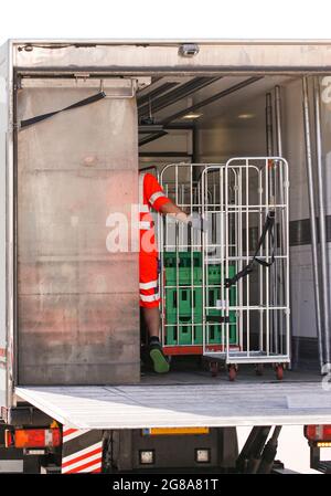 Mann afrikanischer Herkunft in reflektierender Arbeitskleidung, die Milchprodukte aus Kühlwagen in Metallkäfige verladen. Stockfoto