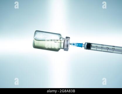 Makro einer hypodermischen Spritze oder Nadel, die mit einem Impfstoff aus der Flasche vor einem blauen Sternhintergrund gefüllt wird Stockfoto