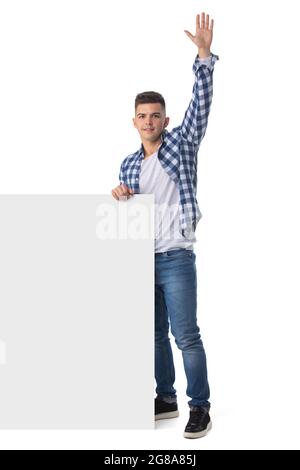 In voller Länge Porträt eines lächelnden jungen, hübschen Mannes mit leerem Banner und winkender Hand Stockfoto