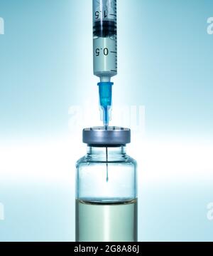Makro einer hypodermischen Spritze oder Nadel, die mit einem Impfstoff aus der Flasche vor einem blauen Sternhintergrund gefüllt wird Stockfoto