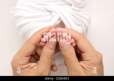 Hände der Eltern. Die Beine des Neugeborenen in den Händen von Mama und Papa. Babies Füße in den Händen. Stockfoto