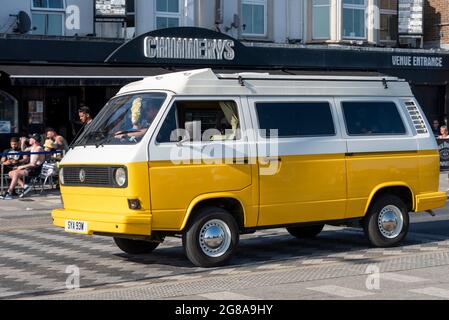 Volkswagen Typ 2 (T3) Transporter in einem hellen Gelb-Weiß-Farbkonzept, der im heißen Sommer entlang der Strandpromenade Marine Parade fuhr Stockfoto