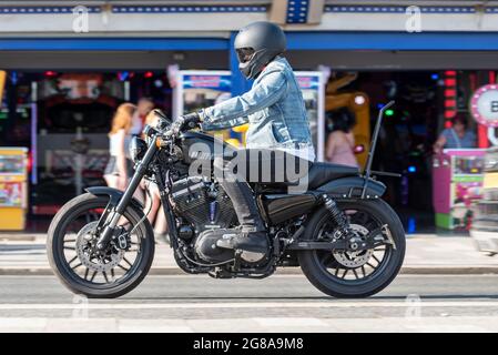 Harley Davidson Motorradfahrer, der an einem heißen Sommertag entlang der Marine Parade in Southend on Sea, Essex, durch die Spielhalle fährt und Denim trägt Stockfoto