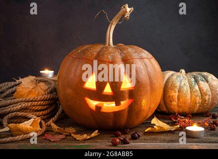 Eine glühende Kürbislaterne, Jacks Kopf auf einem Hintergrund aus Laub, Beeren und Kerzen. Stockfoto