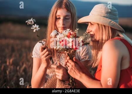 Mutter und Tochter riechen Blumen auf dem Feld. Stockfoto