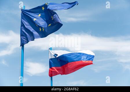 Koper, Slowenien - 12. Juli 2021: Die Flagge der Europäischen Union und Sloweniens wurde auf einem Mast gehisst und flatterte im Wind gegen einen blauen Himmel mit Whit Stockfoto