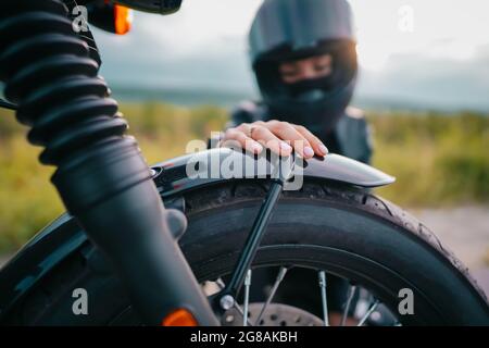 Porträt einer selbstbewussten Motorradfahrerin im Helm, die neben dem Fahrrad sitzt. Junger Fahrer Biker im Freien bei Sonnenuntergang. Stockfoto