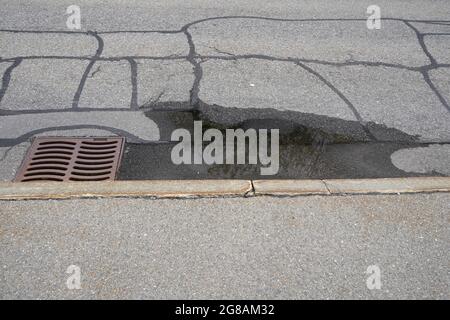 Straße mit einer Schlucht. Es gibt eine Pfütze von Regenwasser, weil es uneben ist. Auf der Straße gibt es Spuren von Reparaturen. Stockfoto