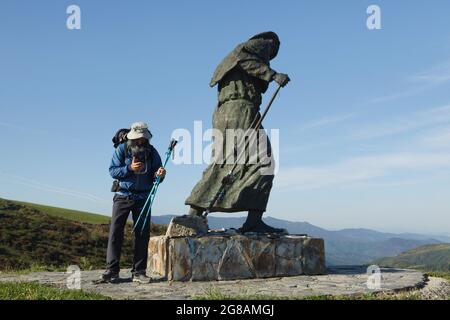 Camino de Santiago (Jakobsweg). Pilger, abgebildet neben der Bronzestatue eines Pilgers auf dem Alto de San Roque in Galicien, Spanien. Die französische Route des Camino de Santiago führt durch diesen Pass, kurz bevor sie das Dorf Hospital da Condesa erreicht. Die Statue des galizischen Bildhauers José María Acuña López wurde 1993 auf dem Pass enthüllt. Stockfoto