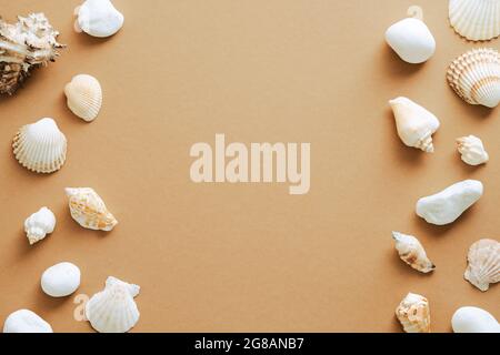 Doppelrahmen aus Muscheln auf sandfarbenem Hintergrund. Flach liegend, Draufsicht, Kopierbereich. Sommer, Urlaubskonzept. Stockfoto