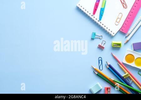 Schulpapier, Farbstifte, Farben, Notizblock auf blauem Tisch. Zurück zum Schulhintergrund. Blick von oben auf den Kinderschreibtisch. Stockfoto