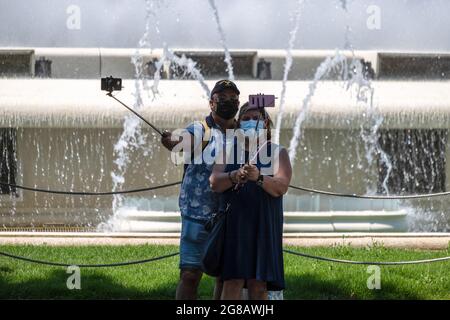 Barcelona, Spanien. Juli 2021. Zwei Menschen sehen sich im Schatten neben den Wasserquellen des Montjüic-Gebirges ein Selfie machen.Laut der Landesmeteorologischen Agentur (AE.MET) wird in Katalonien mit einem Temperaturanstieg gerechnet. Für Barcelona wird die Warnung auf einem orangefarbenen Niveau mit Temperaturen zwischen 30 sein? Und 39? C. Credit: SOPA Images Limited/Alamy Live News Stockfoto