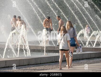 Zwei junge Frauen laufen barfuß am Stadtbrunnen entlang, wo sich die Menschen während der Hitzewelle im Sommer, Park von Sankt Petersburg 300 an, Russland, abkühlen Stockfoto