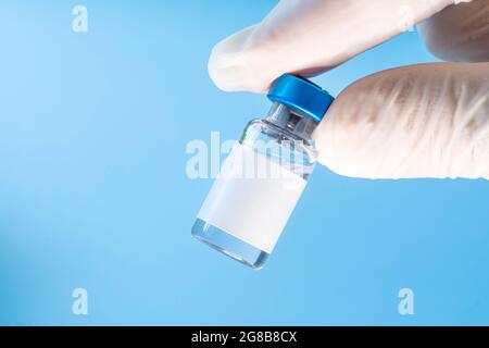 Impfstoff im Fläschchen mit Spritze auf blauem Hintergrund. Leeres weißes Etikett für Design und Text Stockfoto