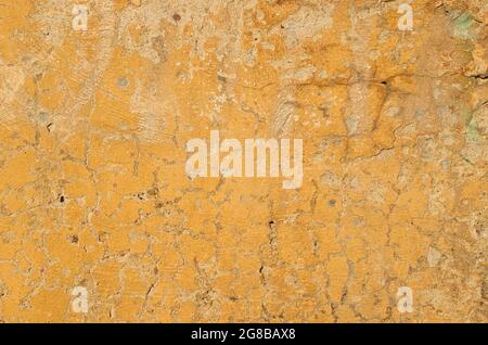 Die Textur der alten rissigen gelben Farbe auf einer Betonwand Stockfoto