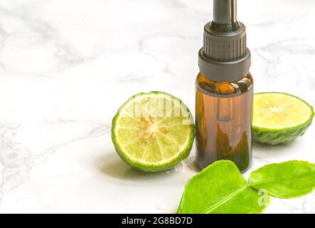 Schöne Verpackung aus ätherischem Bergamotte-Öl in kleiner Glasflasche mit frischer Bergamotte-Frucht mit grünem Blatt auf der Marmorplatte, nass von Wasser. Bla Stockfoto