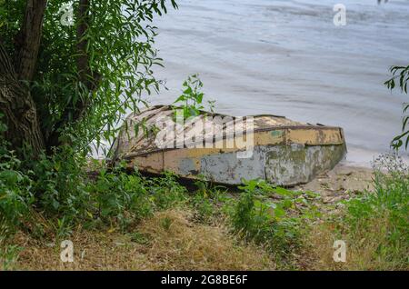Ein altes, ruiniertes Holzboot am Ufer. Ein kleines Fischerboot liegt auf dem Kopf. Stockfoto