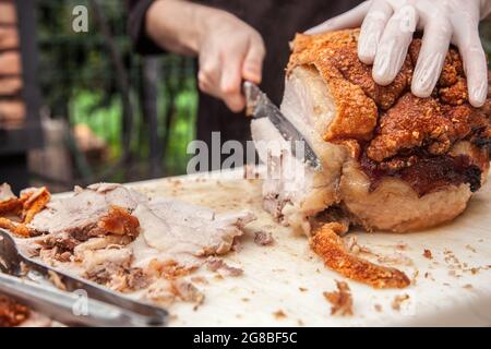 Nahaufnahme der Hände des Küchenchefs, die in einem Restaurantgarten für ein Mittagessen oder einen Brunch typisch italienische gebratene Porchetta aus Schweinefleisch schneiden Stockfoto