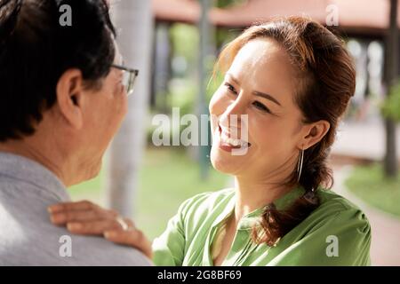Schöne lächelnde alte Frau, die ihrem Mann mit Liebe und Zuneigung entgegensieht, wenn sie im Freien umarmen und tanzen Stockfoto