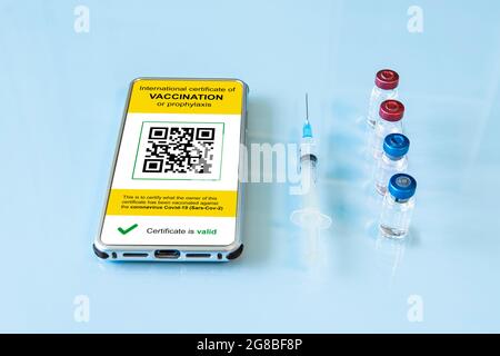 Digitaler Immunitätspass mit einem COVID-19 Impfstempel und qr-Code auf einem Smartphone-Bildschirm mit Impfstoff, Schutzmaske und Spritze auf blauem Bac Stockfoto